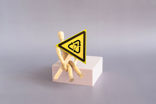 The warning sign &ldquo;Recycling&rdquo; in the form of a yellow triangle on a stand in the hands of a doll. The concept of &ldquo;waste recycling&rdquo;.