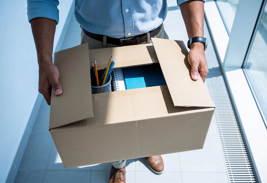 Close up man carrying cardboard box with office supplies after resigning from corporate job in bright modern office