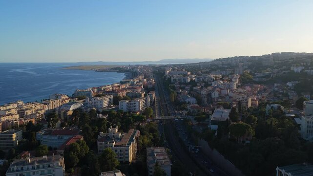 Forward flight along a railway line and busy expressway toward the Baie des Anges and airport runway, hazy golden hour, Nice, French Riviera, Cote d Azur, France