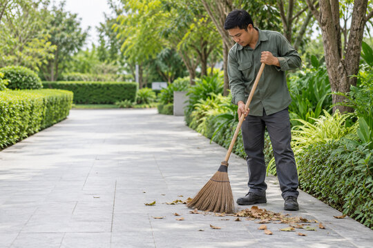 Garden maintenance worker sweeping fallen leaves from a paved walkway