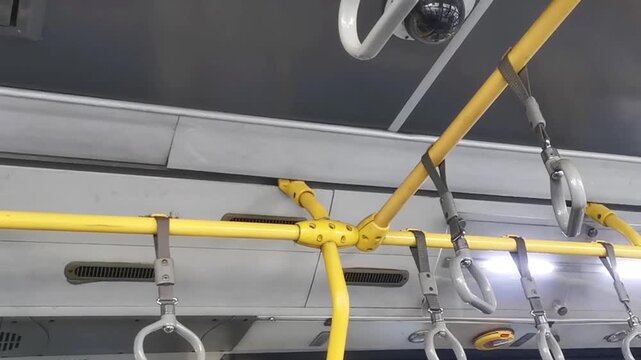 Interior view of yellow handrails and grab handles on a public bus or train with a security camera
