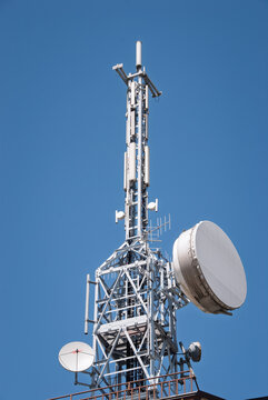 Telecommunications tower with cellular antennas and microwave dishes against a clear blue sky, representing wireless connectivity and digital infrastructure.