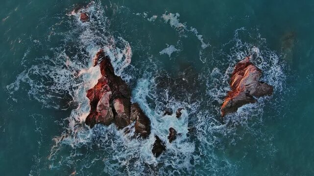 Aerial view of rugged rock formations emerging from the turquoise waters of the Adriatic Sea with white sea foam crashing against the stones in Montenegro.