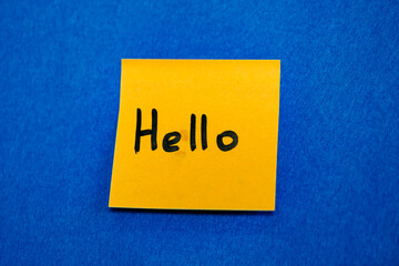 Yellow sticky note with handwritten word Hello on blue background, greeting and friendly communication concept © glebantiy