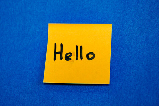Yellow sticky note with handwritten word Hello on blue background, greeting and friendly communication concept
