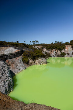View of the vibrant green Devil's Bath geothermal pool surrounded by rocky terrain and a wooden boardwalk at Waiotapu Thermal Wonderland in Rotorua, Waikato Region, New Zealand.