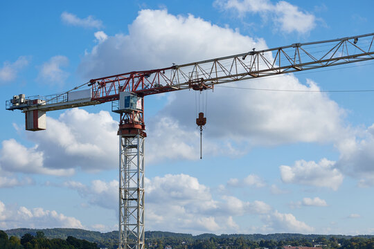 Tower crane construction equipment against blue sky and clouds. Industrial lifting machinery with a long horizontal jib and suspended hook is used for building construction and infrastructure projects
