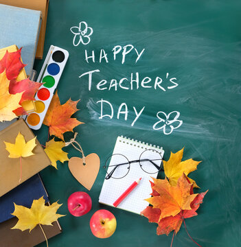 Teacher's day holiday, education concept. chalk inscription "Happy teacher's day" on chalkboard, notebook, school supplies, learning books, eyeglass, apples and autumn leaves on table. top view