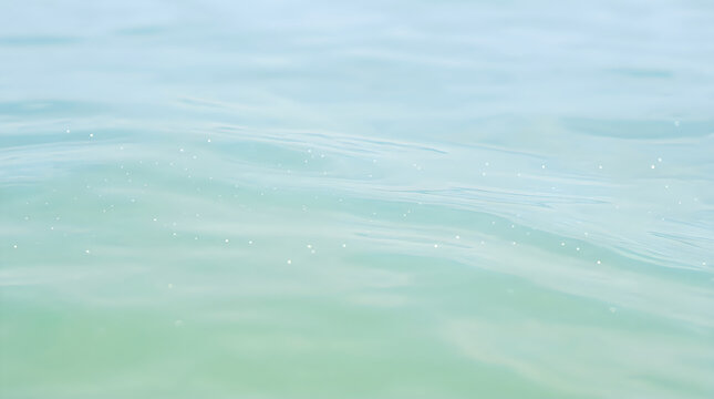 Clear blue ocean water surface with gentle ripples and tiny bubbles reflecting bright sunlight