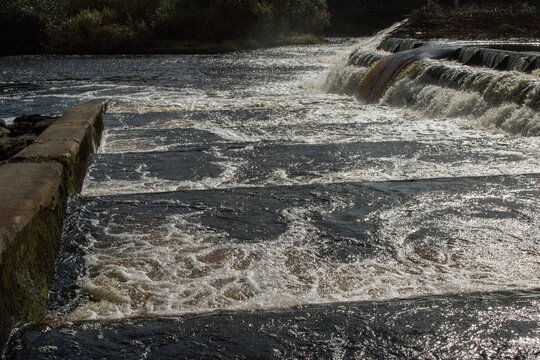 The River Ure cascades over a weir at Boroughbridge in Yorkshire, creating turbulent white water and foam.