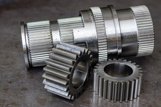 Steel transmission gear hub and spur gears lie on workshop table in close up view.