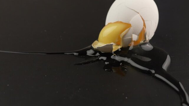 Broken chicken egg with cracked shell yolk falling. egg on black background.