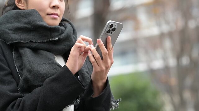 冬の屋外でスマートフォンを操作しながら微笑む30代の日本人女性