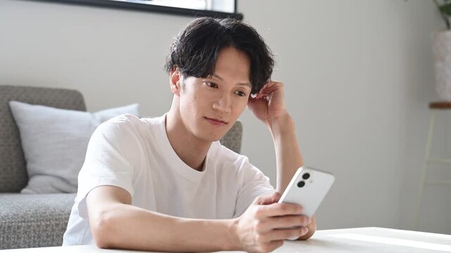 リビングでスマートフォンを見ながらくつろぐ30代の日本人男性