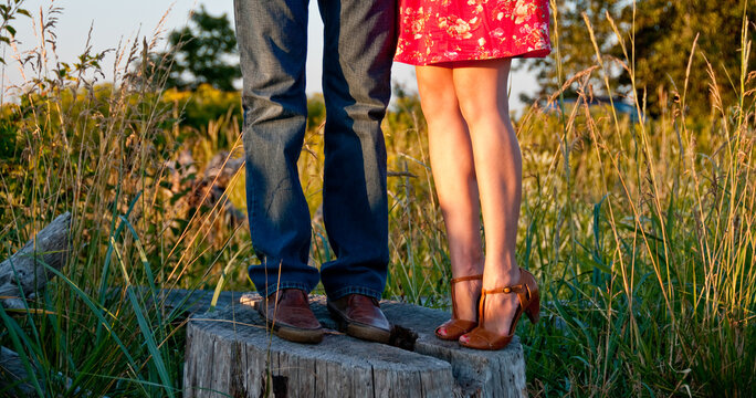 View of a young couple standing on a tree stump in a grassy field during golden hour in Richmond, British Columbia, Canada.
