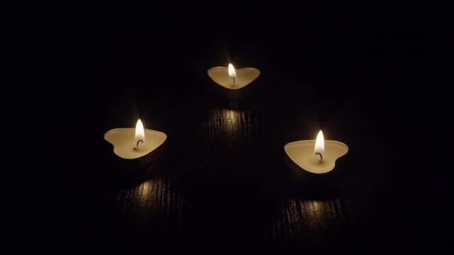 Three heart-shaped candles burning with an even flame on a table in a dark room