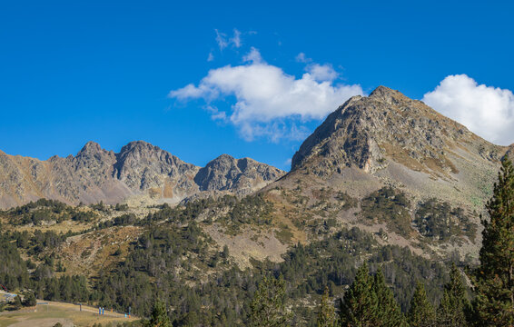 View of the rugged mountain peaks of Llac de Pessons with pine forests and clear blue sky in Grau Roig, Encamp, Andorra.