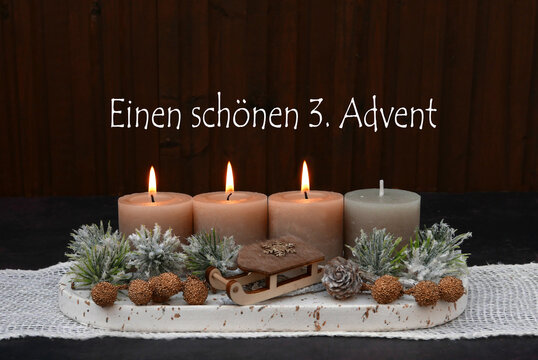 Rustikales Adventsgesteck mit drei brennenden Kerze, Zweigen und Holzschlitten zum 3. Advent.