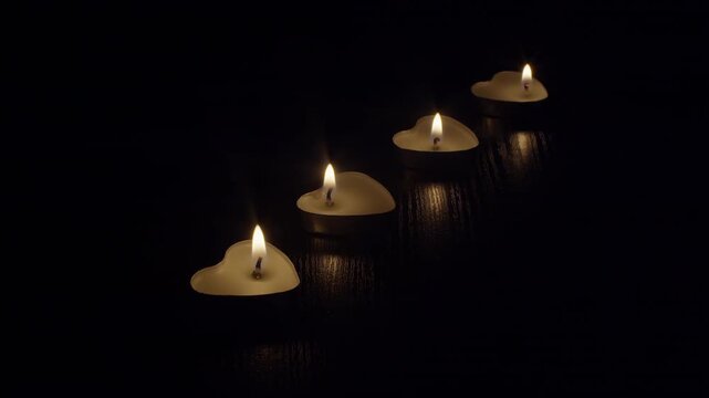 Burning candles in the shape of hearts lined up on a table in a dark room