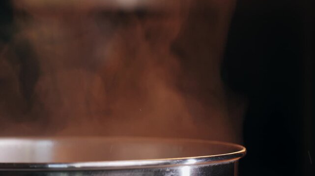 Stainless steel pot on a gas stove with boiling water and steam, cooking soup