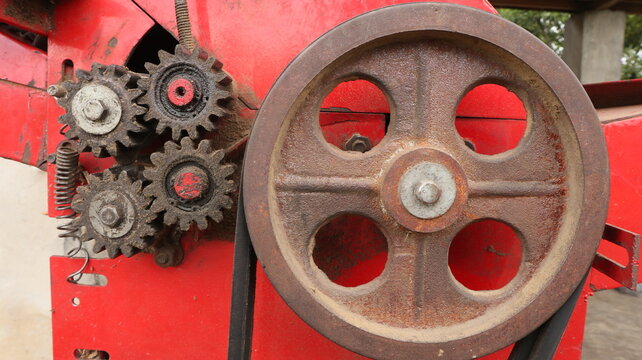Close-up view of mechanical gears, pulley, belt, and springs on a red corn threshing machine used for agricultural processing