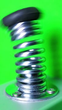 Close up of a silver metal spring door stop vibrating and wobbling rapidly against a bright green screen background