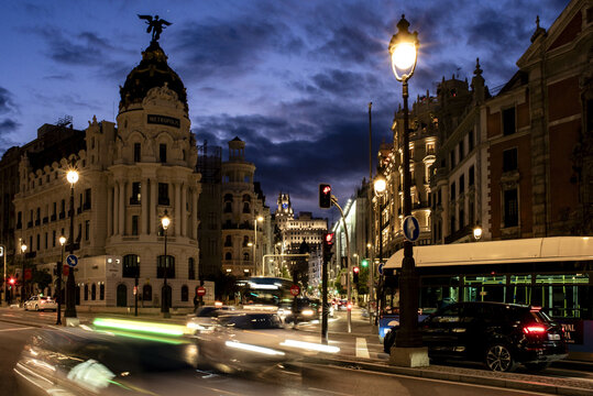 View of the Metropolis Building illuminated at night with light trails from passing traffic on the streets of Madrid, Community of Madrid, Spain.
