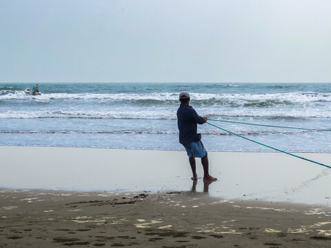 Man fishing with a long line while standing at the water's edge on a sandy beach