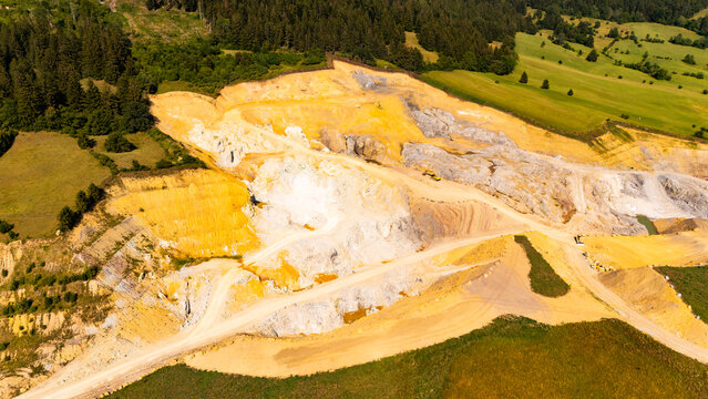 Quarry benches form terraces beside farmland and forest.. White and yellow cut faces rise above curving access tracks at the forest edge.