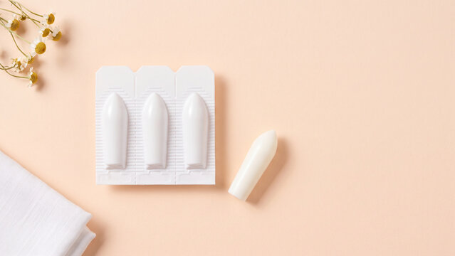 Suppositories in White Blister Pack with Chamomile Flowers and Linen Cloth on Peach Background, Flat Lay with Copy Space