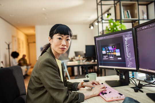 Graphic designer edits app interface on dual monitors in office