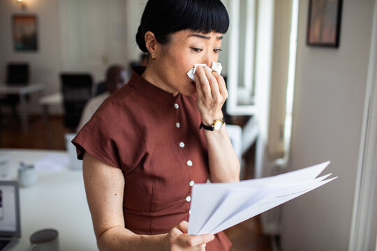 Concerned woman blowing nose while reading paperwork in office