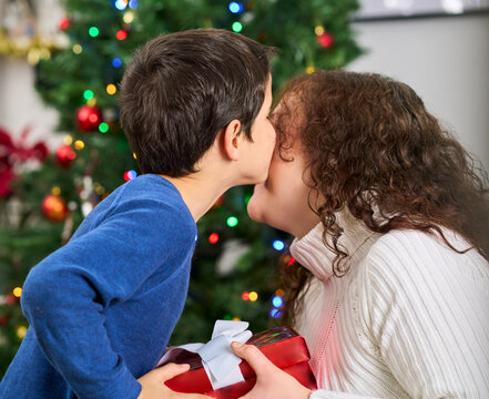 Son, christmas day gift and kiss on couch in living room of home for love, celebration or surprise. Son giving his mother a kiss as a Christmas gift.