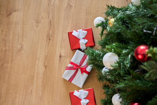 Beautifully wrapped Christmas gifts and  Christmas crackers placed beside a Christmas tree. Christmas background with decorations and gift boxes on wooden floor at home.
