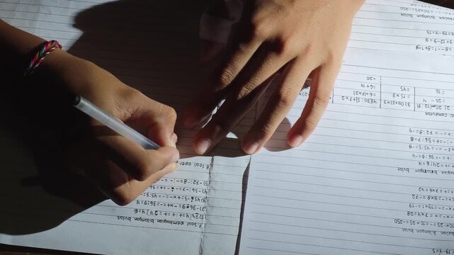 Student writing math homework and solving equations in a notebook at night