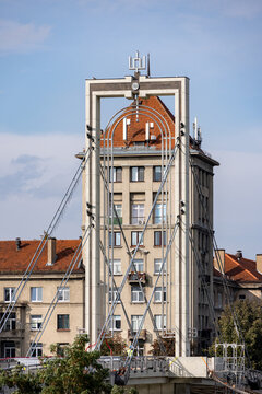 View of the M. K. Ciurlionis Bridge with its distinctive pylon structure and cable stays set against a historic building with a red tiled roof in Kaunas, Kaunas County, Lithuania.