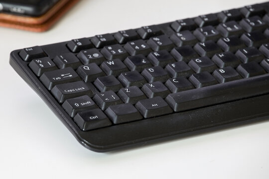 Used Black Desktop Keyboard with Shiny Keycaps from Heavy Use. Selective focus highlights the central keys, revealing a smooth and glossy patina caused by continuous daily typing and hard work.