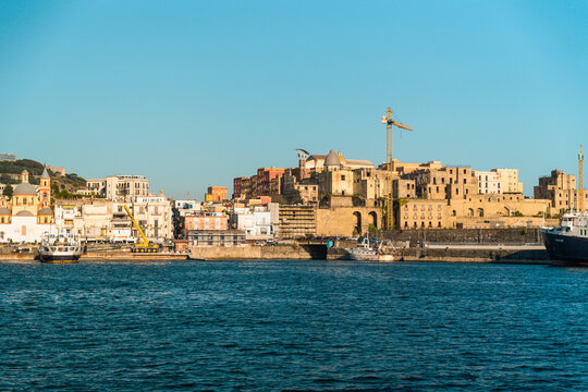 View of the historic Naples waterfront with traditional buildings, a prominent church dome, construction cranes, and boats docked in the harbor in Naples, Campania, Italy.