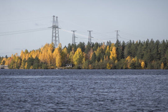 View of power lines stretching across a forest with autumn foliage along the riverbank in Rovaniemi, Lapland, Finland.