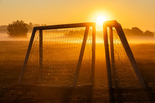 View of a soccer goal standing in a misty field during a golden sunrise in Herlufmagle, Sjaelland, Denmark.