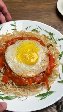 Vertical video of serving American chopsuey with crispy noodles and fried egg on table
