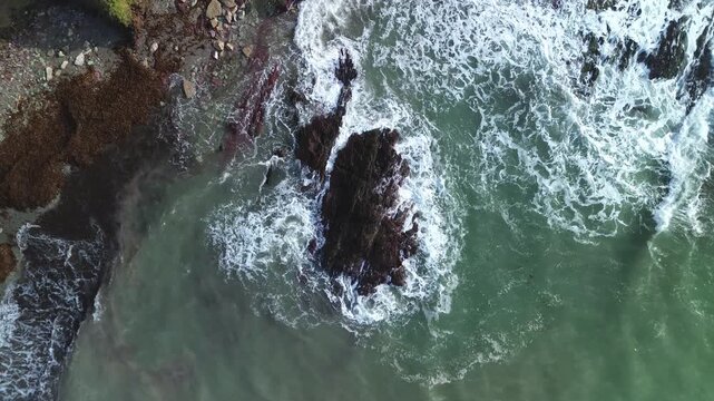 Aerial view of Talland Bay rocky outcrop with waves crashing against the shore in Looe, Cornwall, United Kingdom.