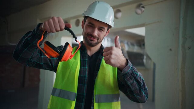 Cheerful Caucasian electrician man showing thumb up wearing safety earmuffs factory male guy technician builder engineer recommend acoustic headphones protection handyman architect approving equipment