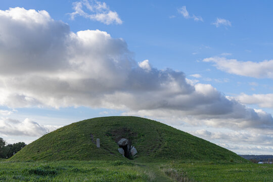 View of the Neolithic passage grave Kong Asgers Hoj set in a grassy mound under a blue sky with clouds in Stege, Mon, Denmark.