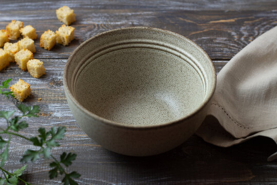 Empty rustic ceramic bowl with golden croutons, parsley and linen napkin on weathered wood, styled for soup and savory meals