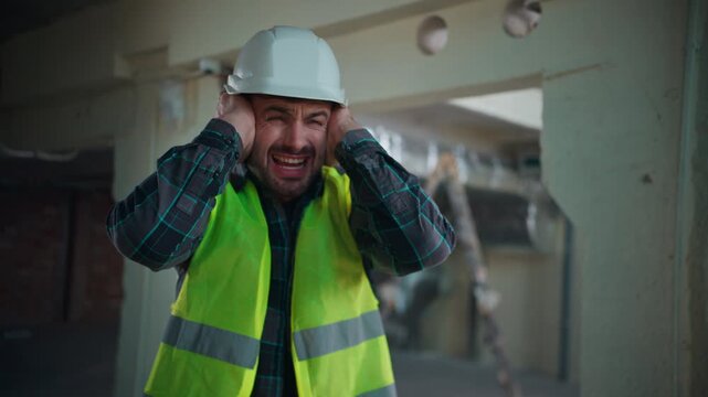 Caucasian builder man covering ears with hands avoiding loud explosion noise construction worker male in hardhat uniform handyman engineer hiding industrial factory demolition sound safety protection