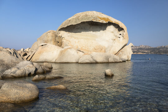 View of Spiaggia Testa del Polpo, a unique rock formation resembling an octopus head, surrounded by clear turquoise water and coastal rocks in La Maddalena, Sardinia, Italy.