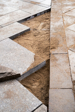 Sidewalk renovation reveals sand foundation beneath removed paving slabs. Old pavement sections dismantled before installation of new stone tiles.