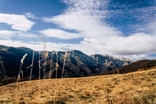 View of the Golyam Kademliya Shelter area in the Balkan Mountains with dry autumn grass in the foreground and snow-capped peaks under a blue sky in Stara Zagora, Bulgaria.