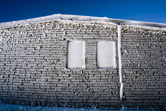 View of the Golyam Kademliya Shelter brick wall covered in thick rime ice and snow under a clear blue sky in Stara Zagora, Bulgaria.
